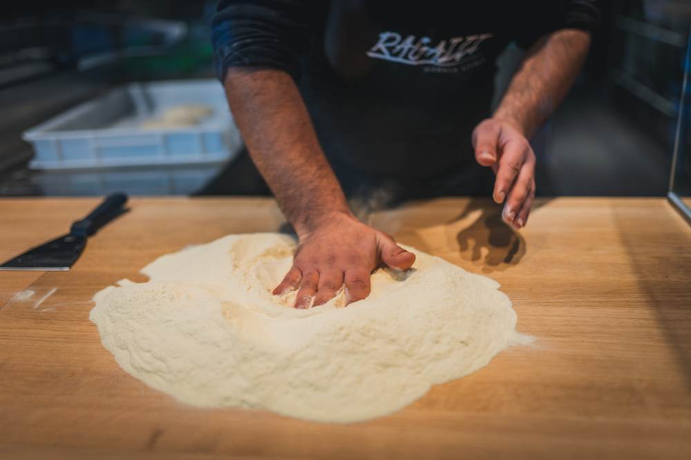 Hände arbeiten Mehl in den Pizzateig ein